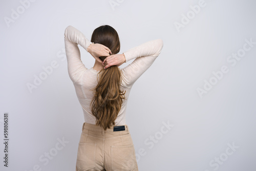 Young woman with strong healthy long hair, making a ponytail on white background, back view photo