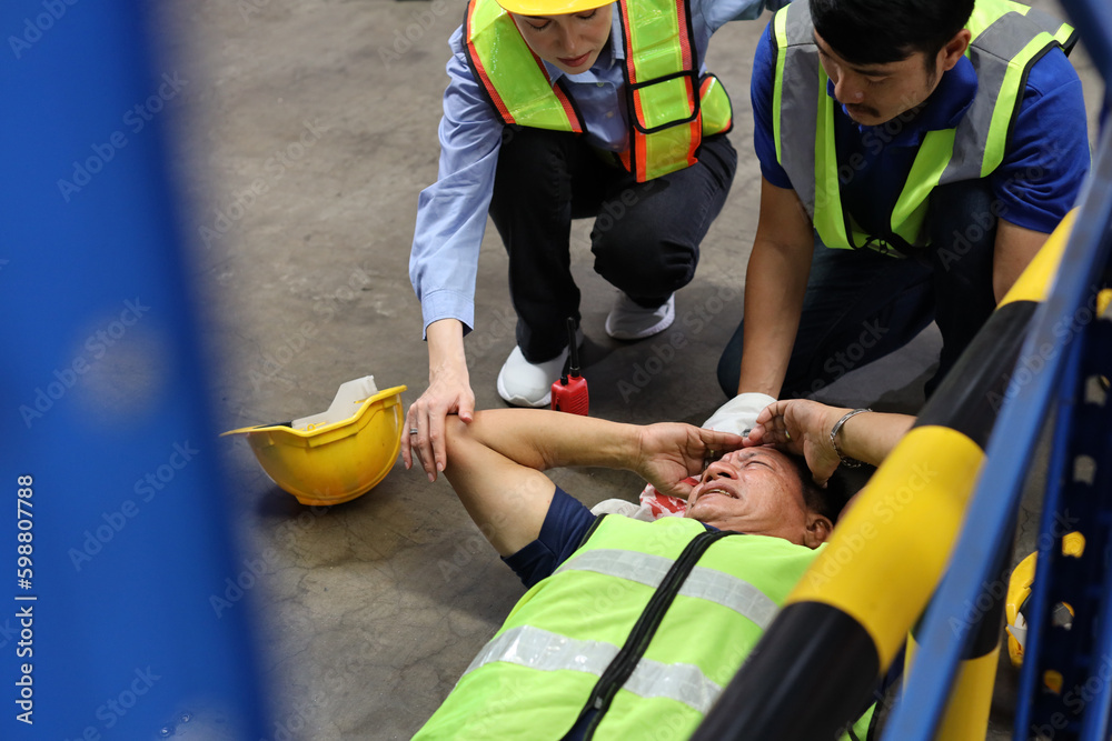 Safety colleagues team helping middle aged warehouse asian worker who had broken head accident and lying on the floor in warehouse while using walkie talkie radio. First aid training concept. Safety colleagues team helping middle aged warehouse asian worker who had broken head accident and lying on the floor in warehouse while using walkie talkie radio. First aid training concept.