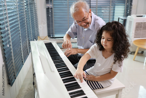 Happy smiling asian senior man sitting and playing piano while teaching grandchild in living room house indorrs. Musical and relaxation makes elder male happiness. Health care lifestyle concept.