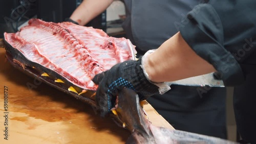 Close-up of the process of cutting tuna fish at the market. Male hands in gloves cutting a large fish with a knife. Generative AI