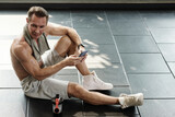 Man tired after morning workout sitting on floor and checking smartphone