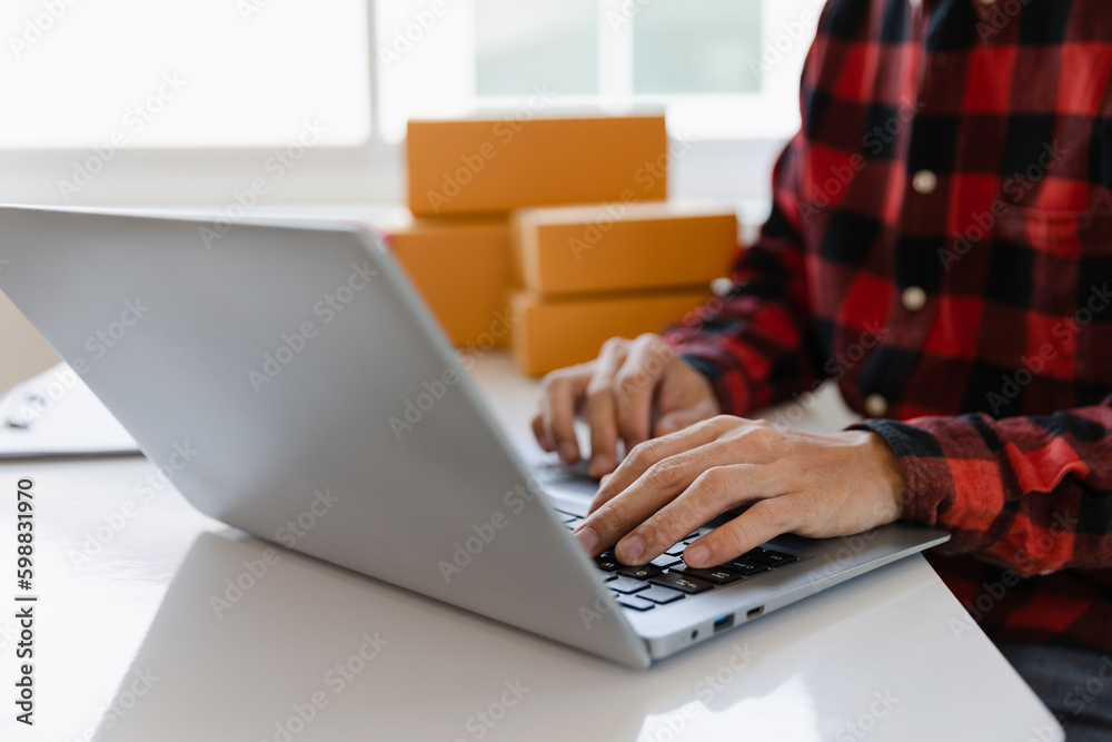 Fototapeta premium Asian freelance male SME small business entrepreneur working from home Use smartphones and laptops for commercial inspections. online marketing Packaging boxes, SME sellers, concepts, e-commerce teams