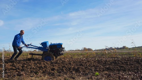 a man plows with a walk-behind tractor,a farmer plows a field in the fall with a plow, following a two-wheeled tractor, a man works in the field photo