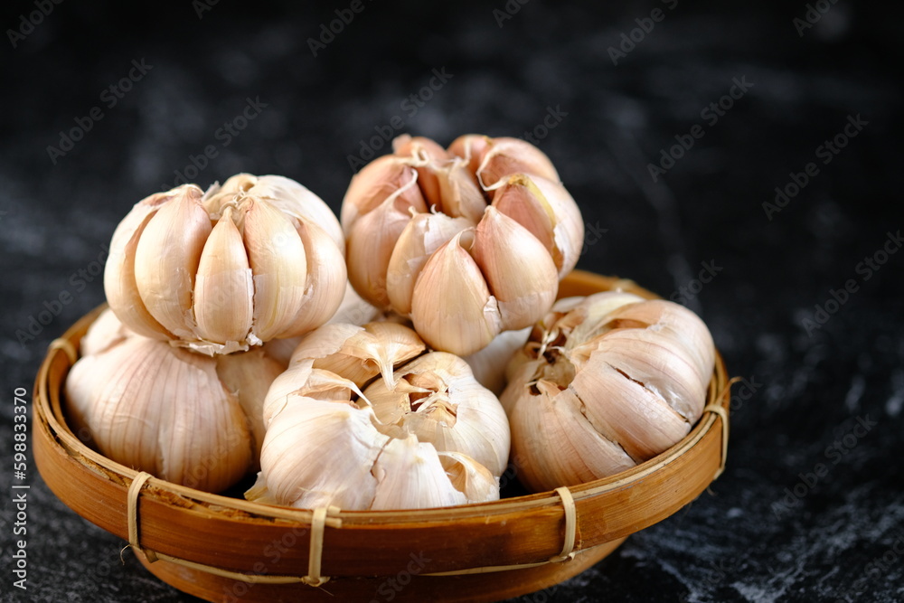 Fototapeta premium a whole pile of garlic in a woven bamboo basket on the black marble. Garlic is commonly used as a food ingredient in the Mediterranean region, as well as a common spice in Asia, Africa, and Europe.