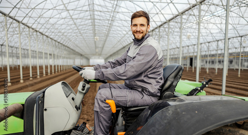 Fotografie An agronomist is sitting on tractor and cultivating the land in hothouse