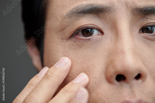 Closeup image of man applying anti-wrinkle eye cream in the morning