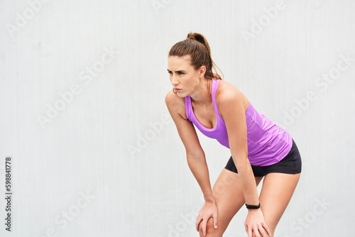 Working up a sweat. an attractive young female athlete down on her haunches after a workout against a grey background.