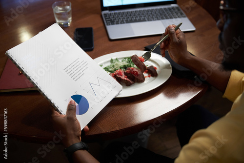 Close-up of African American man examining business contract while having lunch at table in restaurant