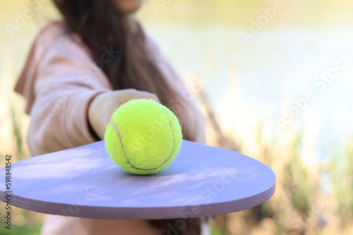 Summer or spring games. Women's hands with a wooden racket and a green ball close-up. Outdoor sport leisure activity. Green tennis ball on a racket. © Mariia