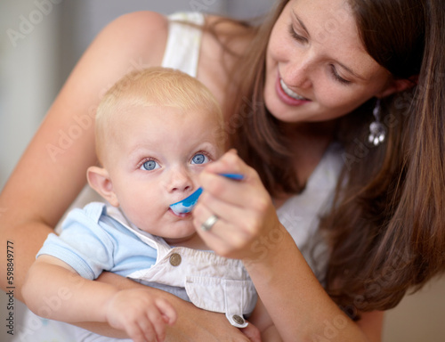 Yoghurt tastes good. A cute toddler being fed by his mother while sitting on her lap.