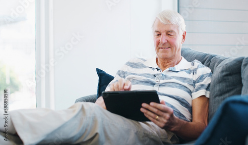 Connect to stay current. a senior man using a digital tablet on the sofa at home.