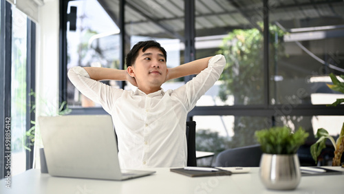 Relaxed Asian businessman putting his arms behind his head to relax after finishing work.