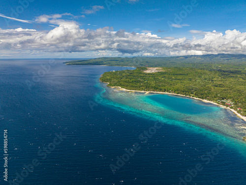 A body of land surrounded by Beautiful waves in outstanding blue ocean with a long white sandy beach. Siquijor, Philippines.