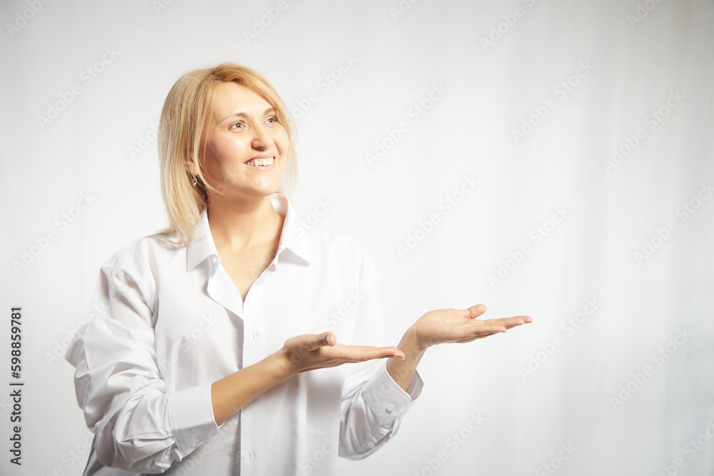 Portrait of a pretty blonde smiling woman posing on a white background and pointing somewhere. Happy girl model in white shirt in studio. Copy space Portrait of a pretty blonde smiling woman posing on a white background and pointing somewhere. Happy girl model in white shirt in studio. Copy space