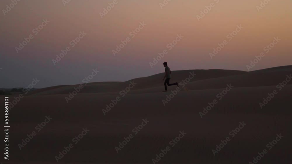 Slow motion silhouette shot of an Indian man running on the top of the sand dunes of the Thar desert at Jaisalmer in Rajasthan, India. Tourist runs in slow motion in the desert with copy space. Slow motion silhouette shot of an Indian man running on the top of the sand dunes of the Thar desert at Jaisalmer in Rajasthan, India. Tourist runs in slow motion in the desert with copy space.