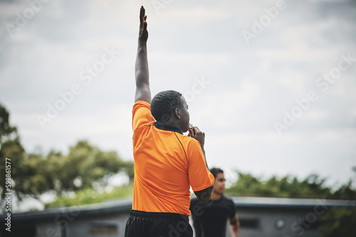He shoots and scores. a referee blowing his whistle while lifting his hand up in the middle of a rugby match on a field during the day. photo