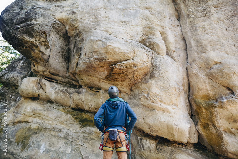 Strong climber with equipment on a belt holding rope and preparing to