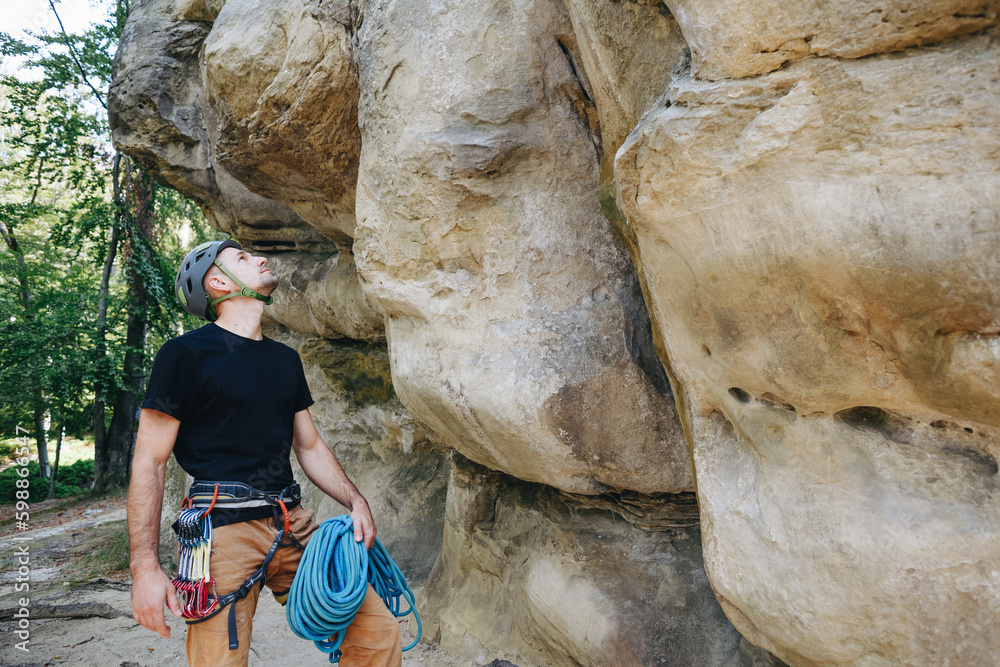 Strong climber with equipment on a belt holding rope and preparing to