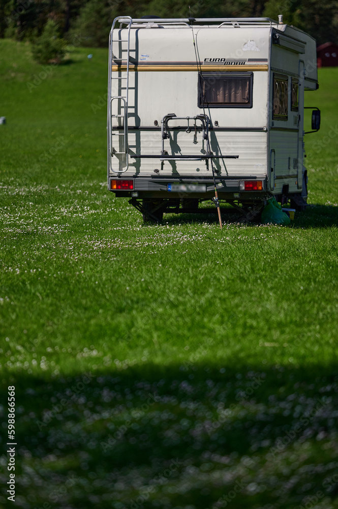 old school white camper parked on the grass by the lake. A vintage house on wheels in a sunny aura.