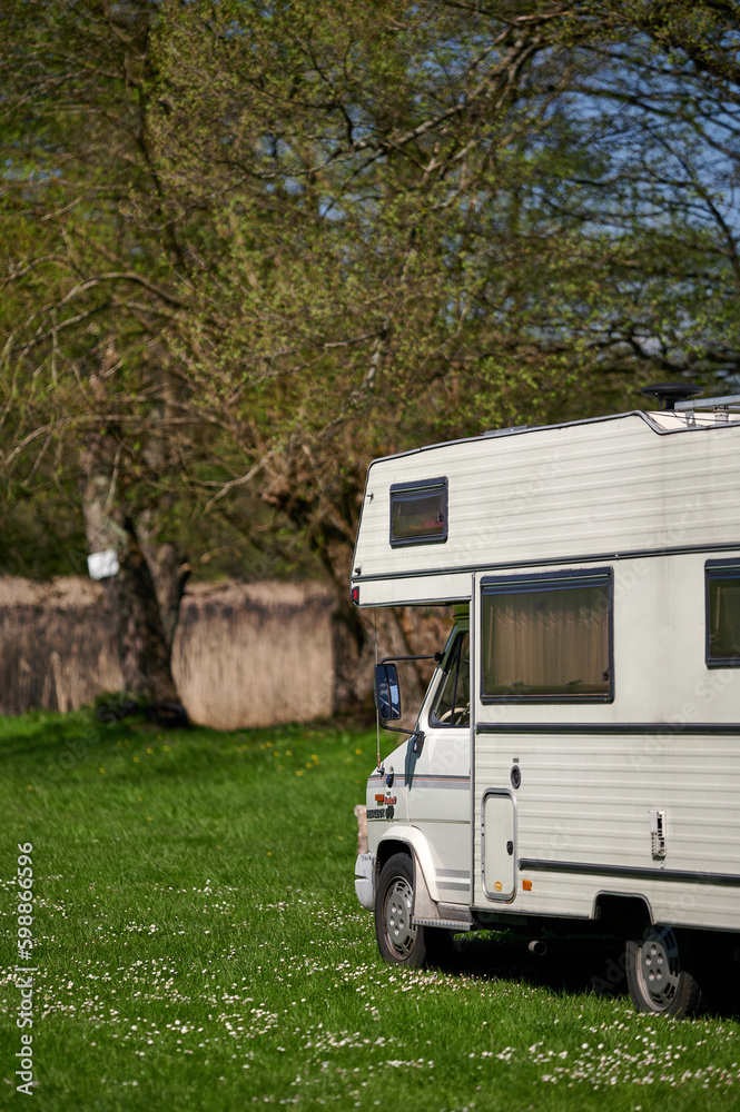 old school white camper parked on the grass by the lake. A vintage house on wheels in a sunny aura. old school white camper parked on the grass by the lake. A vintage house on wheels in a sunny aura.