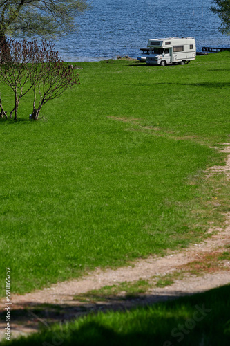 Obraz na płótnie old school white camper parked on the grass by the lake. A vintage house on wheels in a sunny aura. w salonie