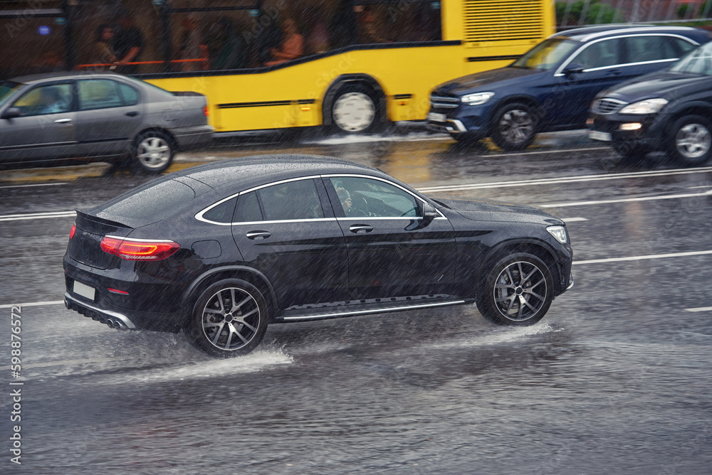 Car driving fast on wet road, driving through puddle during heavy rain. Car driving on flooded asphalt road. Dangerous driving conditions, wet road risk of aquaplaning. Slippery road, low visibility