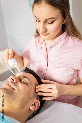 Beautician doing face treatment in beauty salon to a man.