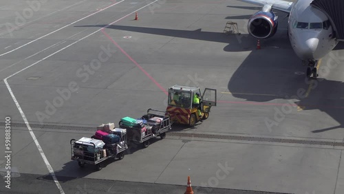 Trailer truck full of suitcases on the runway. Workers carry suitcases to load on the plane.