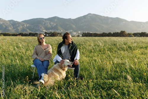 Wallpaper Mural Young happy couple with dog, sitting on chairs in feather grass field on summer sunset day Torontodigital.ca