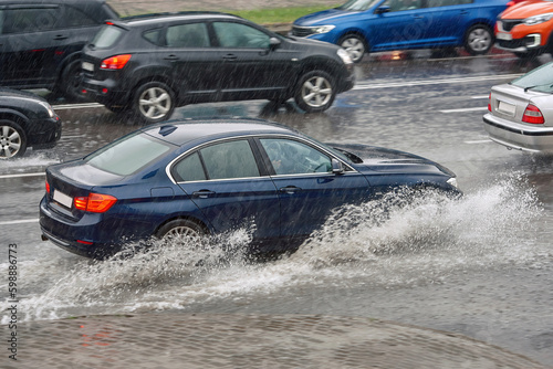 Obraz na płótnie Car splash water while driving on wet road, driving through puddle during heavy rain. Car driving on flooded asphalt road. Dangerous driving conditions, wet road risk of aquaplaning. w salonie
