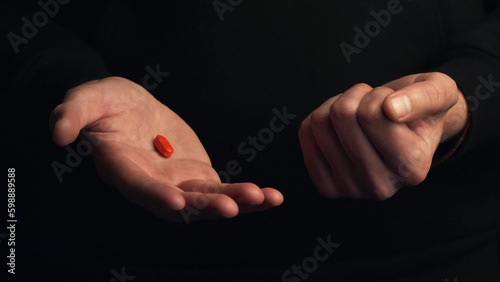 Studio shot hands show red pill isolated on black background. Concept of making right choice.