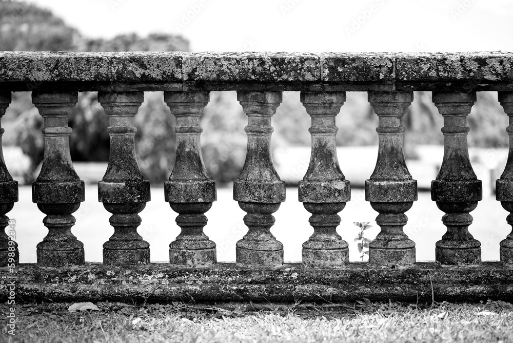 Balustrade railing of natural stone or rock supported by balusters forming an ornamental parapet to the balcony or terrace of a historic villa in Saint Pierre Martinique, black and white grey scale.