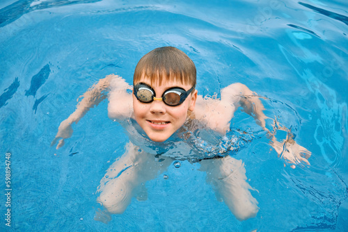 Smiling boy portrait in swimming goggles, Child swim in the pool, sunbathes, swimming in hot summer day. Relax, Travel, Holidays, Freedom concept. 