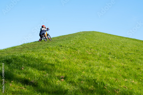 A little boy is trying to climb the hill on his bike. Child development, cycling and children cycling. educational and development activities. Activities in nature. Perseverance and determination.