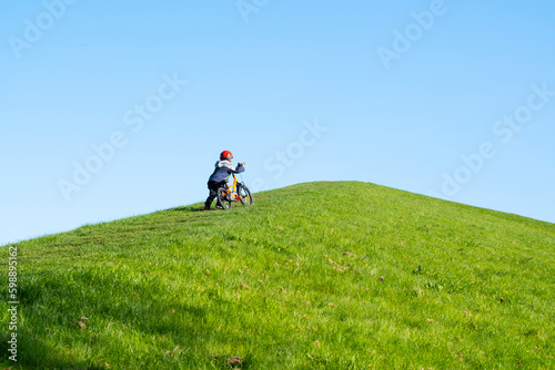 Fotografía A little boy is trying to climb the hill on his bike