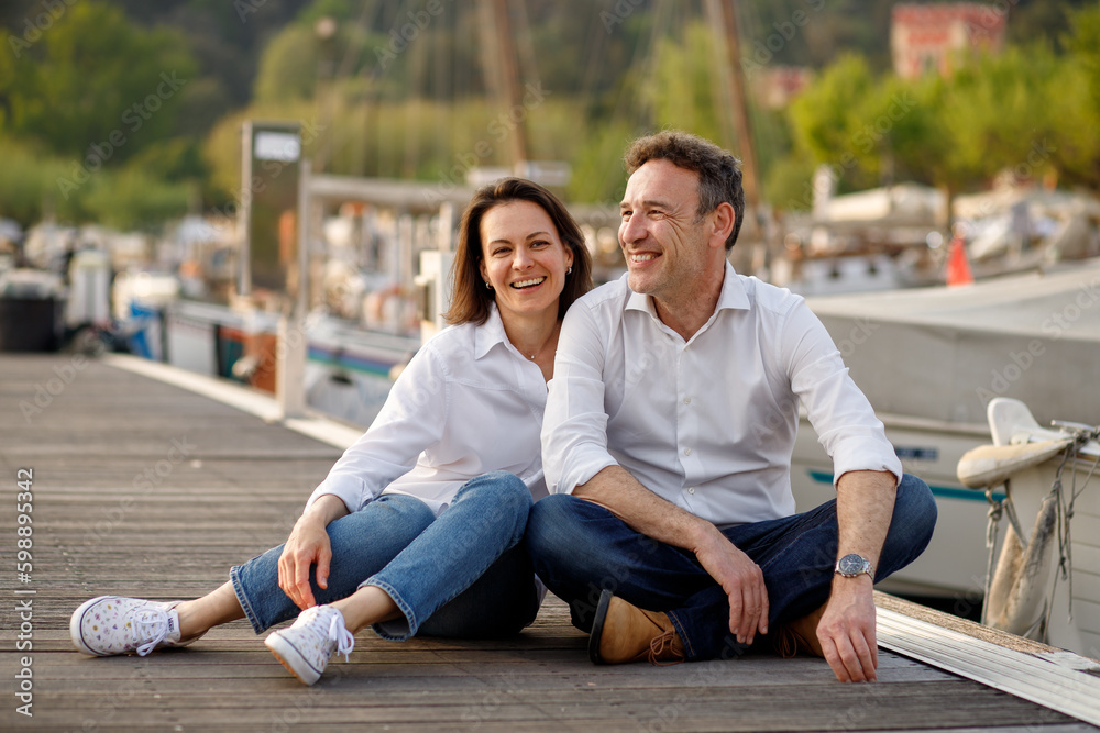 Stylish couple in love in white shirts sitting and smiling at the wooden pier at Italian Garda lake Stylish couple in love in white shirts sitting and smiling at the wooden pier at Italian Garda lake