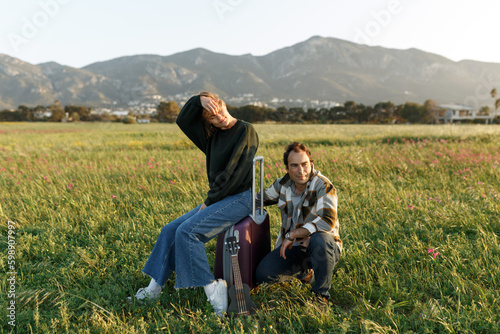 Picture of female and male holding hands, sitting on suitcase on the field outdoors