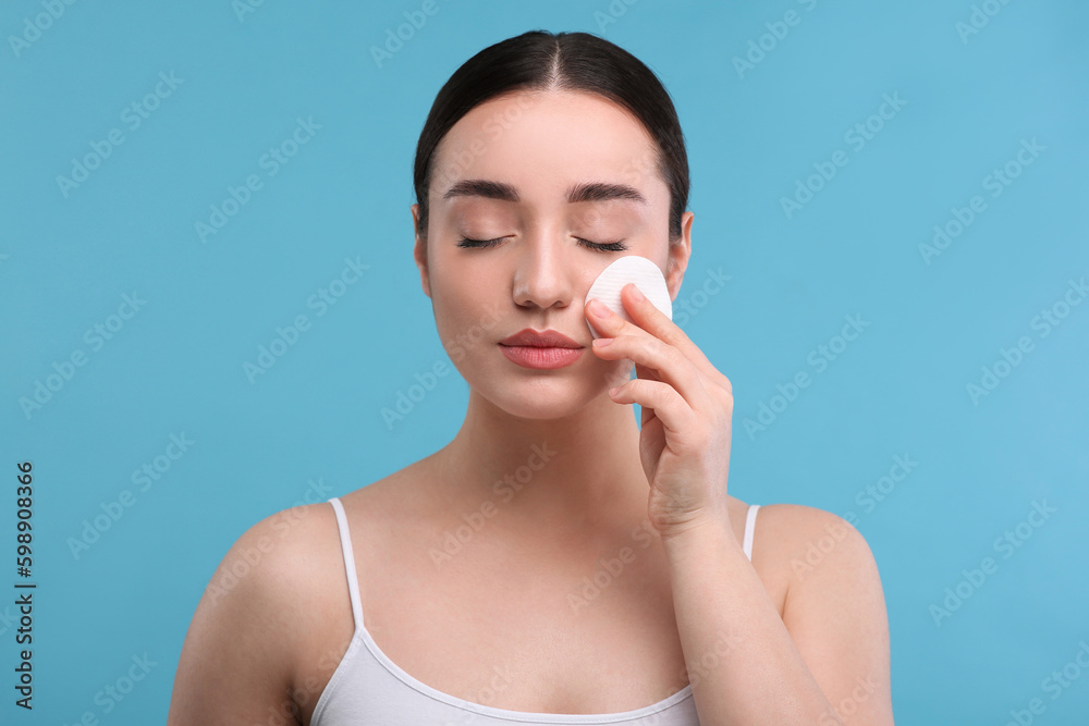 Beautiful woman removing makeup with cotton pad on light blue background Beautiful woman removing makeup with cotton pad on light blue background