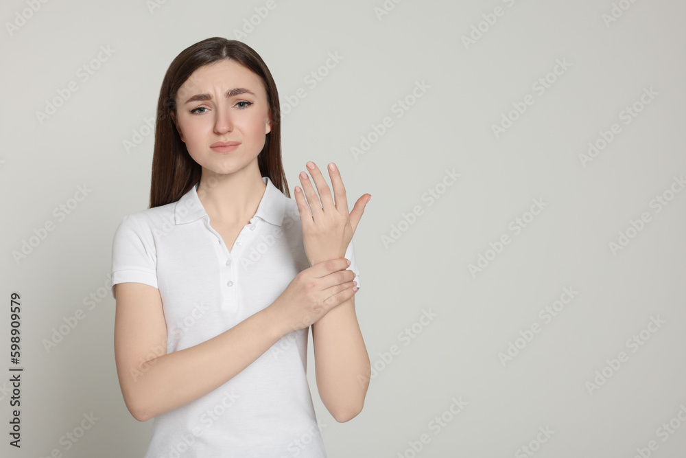 Young woman suffering from pain in her hand on light grey background, space for text. Arthritis symptoms Young woman suffering from pain in her hand on light grey background, space for text. Arthritis symptoms