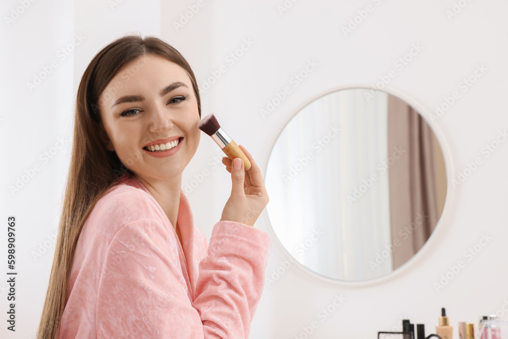Beautiful young woman applying makeup with brush indoors Beautiful young woman applying makeup with brush indoors