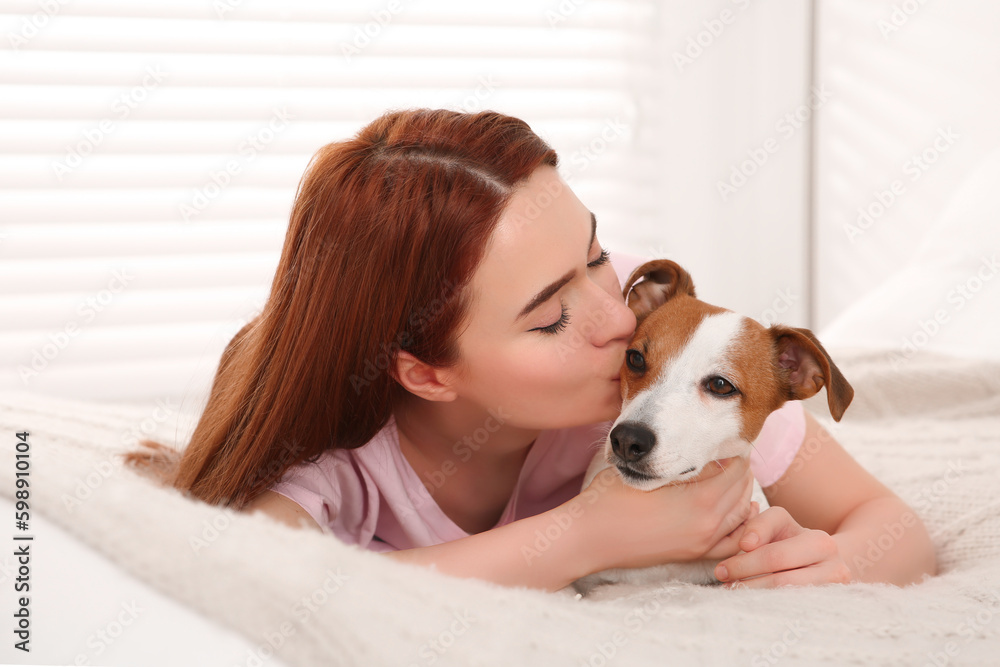 Woman kissing cute Jack Russell Terrier dog on bed at home