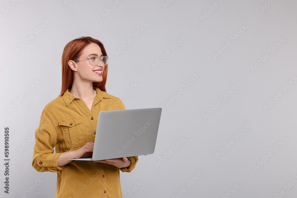 Smiling young woman working with laptop on grey background, space for text Smiling young woman working with laptop on grey background, space for text