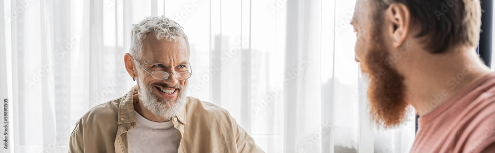 Senior gay man smiling at blurred partner at home, banner. 