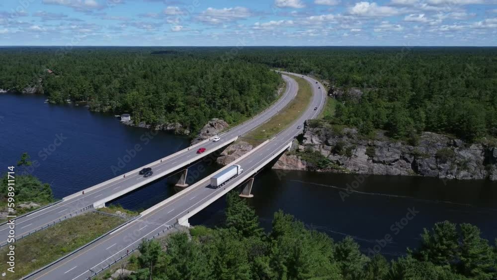 Rising aerial shot of curved highway bridge over lake through rock and trees near Gravenhurst Ontario Rising aerial shot of curved highway bridge over lake through rock and trees near Gravenhurst Ontario
