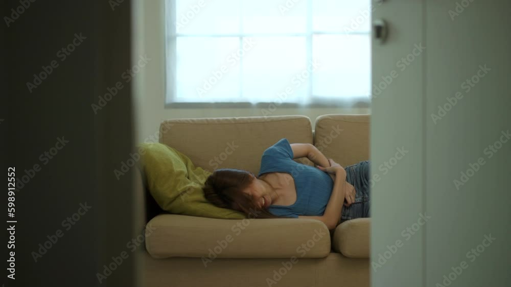 Unhappy painful moment Young woman suffering from stomach ache or period cramps on sofa in living room. Female abdominal pain, gastritis, and painful periods at home. Healthcare concept. Unhappy painful moment Young woman suffering from stomach ache or period cramps on sofa in living room. Female abdominal pain, gastritis, and painful periods at home. Healthcare concept.