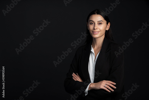 Portrait of smiling business woman with cross hands in formal suit on black background. Beautiful girl