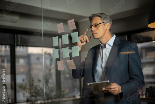 Portrait of successful businessman in office. Man writing ideas on colorful stickers on glass wall