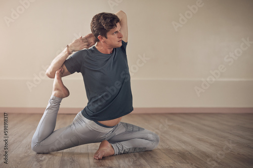 Pushing my body to the next level. Full length shot of a handsome young man holding a mermaids pose during an indoor yoga session alone.