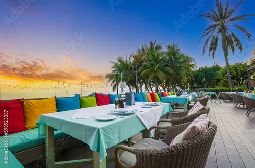 Seaside restaurant,Beach club concept, food corner or cafe, restaurant tables, straw natural chairs, wooden tables, makrome knitted sun umbrellas, white modern sun beds, sea view on background