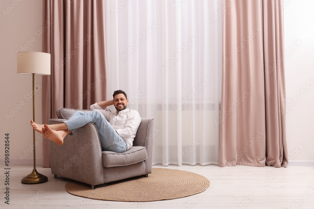Happy man resting on armchair near window with beautiful curtains at home. Space for text Happy man resting on armchair near window with beautiful curtains at home. Space for text